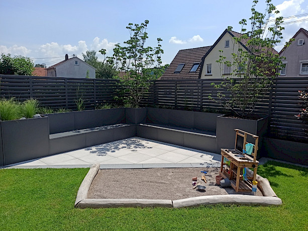 Sandkasten auf Rasen und dreieckige Stelle mit Bank